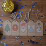 All five cross stitched tags featuring a Christmas tree, robin, angel, Santa and snowman laid side by side on a table