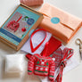 Contents of cross stitch Christmas jumper kit including letterbox packaging, stuffing, white aida, ribbon, threads, ribbon and red felt