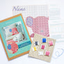 Kit contents for pink teddy cross stitch kit including pattern, fabric and threads.