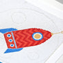 Close up of red and blue moon rocket cross stitched