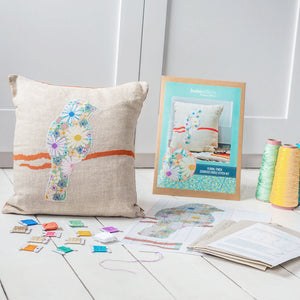 Flower filled bird cross stitch kit materials including threads, pattern and fabric alongside made up finch cushion