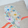 Close up of colourful cross stitched bird design filled with flowers sitting on an orange branch