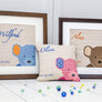 Three colourways of the peeping ted cross stitch kit shown framed or as a cushion, pink, blue and brown