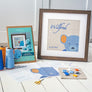 Blue teddy cross stitch design shown framed with threads, pattern and fabric