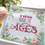 Banner which says This Took me Ages in cross stitch surrounded by flowers
