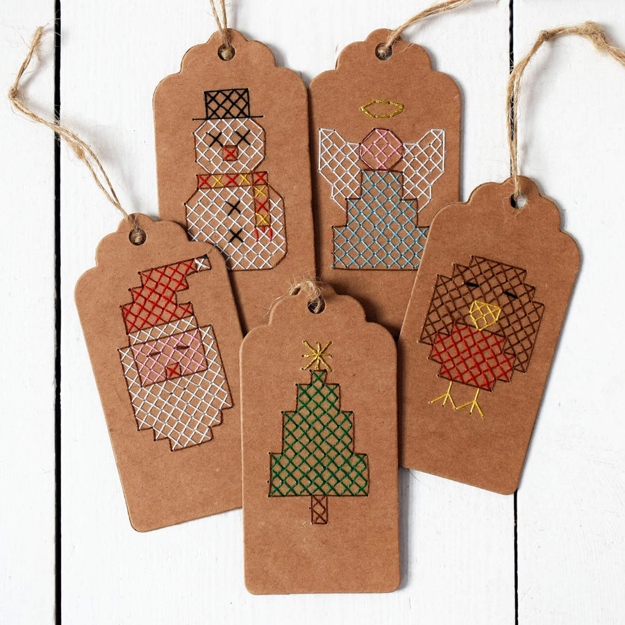 Five designs of Christmas gift tags cross stitched and placed together on a wooden floor