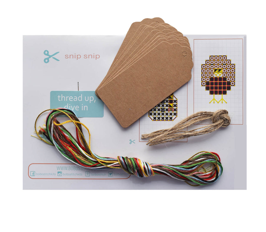 Contents of cross stitch gift tag kit including pattern, tags, hanging twine needle and threads.