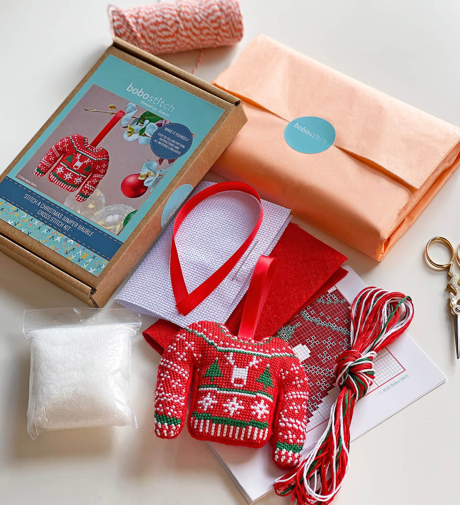 Contents of cross stitch Christmas jumper kit including letterbox packaging, stuffing, white aida, ribbon, threads, ribbon and red felt