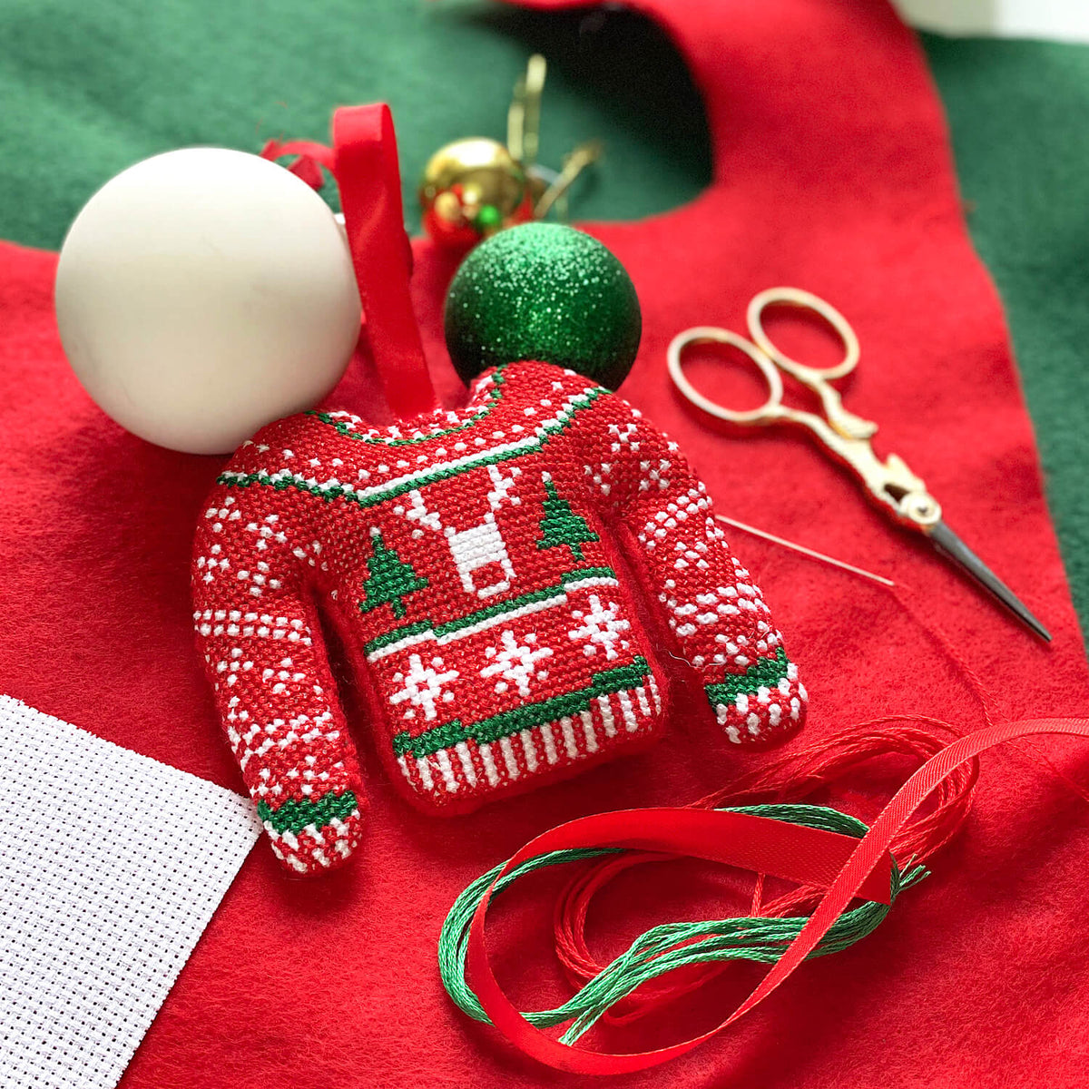 Finished cross stitch Christmas jumper bauble amongst kit materials including felt, aida and ribbon