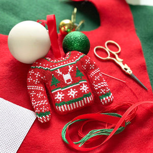Finished cross stitch Christmas jumper bauble amongst kit materials including felt, aida and ribbon