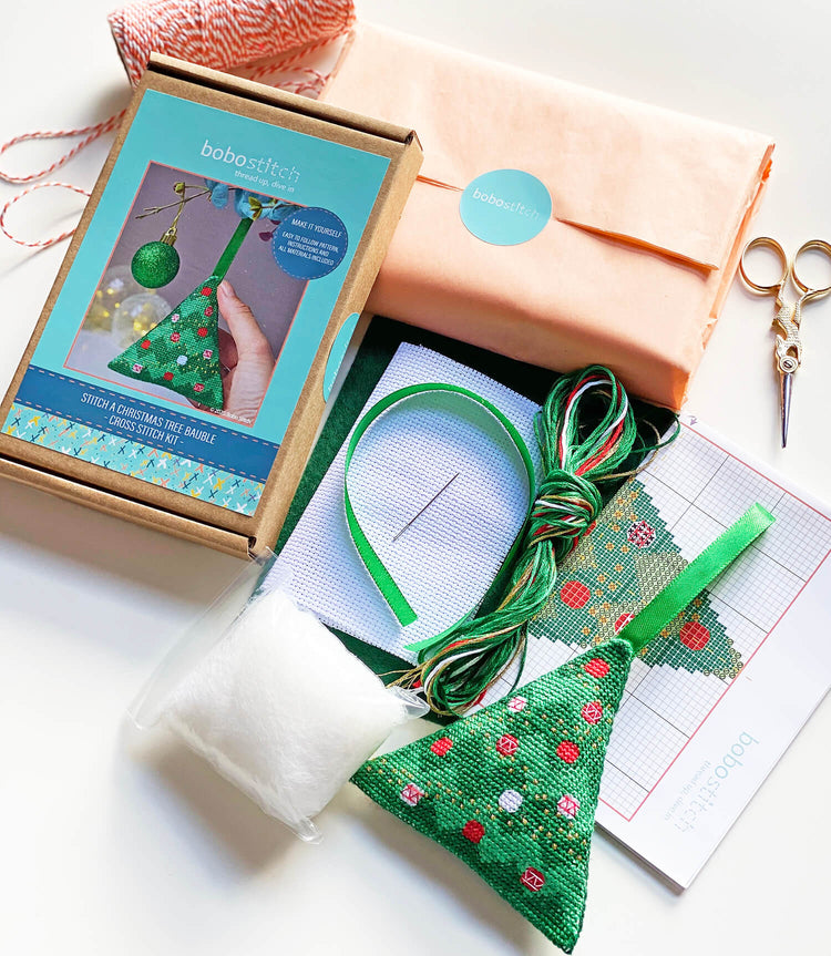 Contents of kit to make cross stitch Christmas tree decoration including pattern aida, threads, stuffing, green felt and green ribbon.