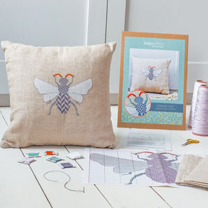 Contents of cross stitch kit including packaging, instructions, thread and fabric, shown with made up cushion