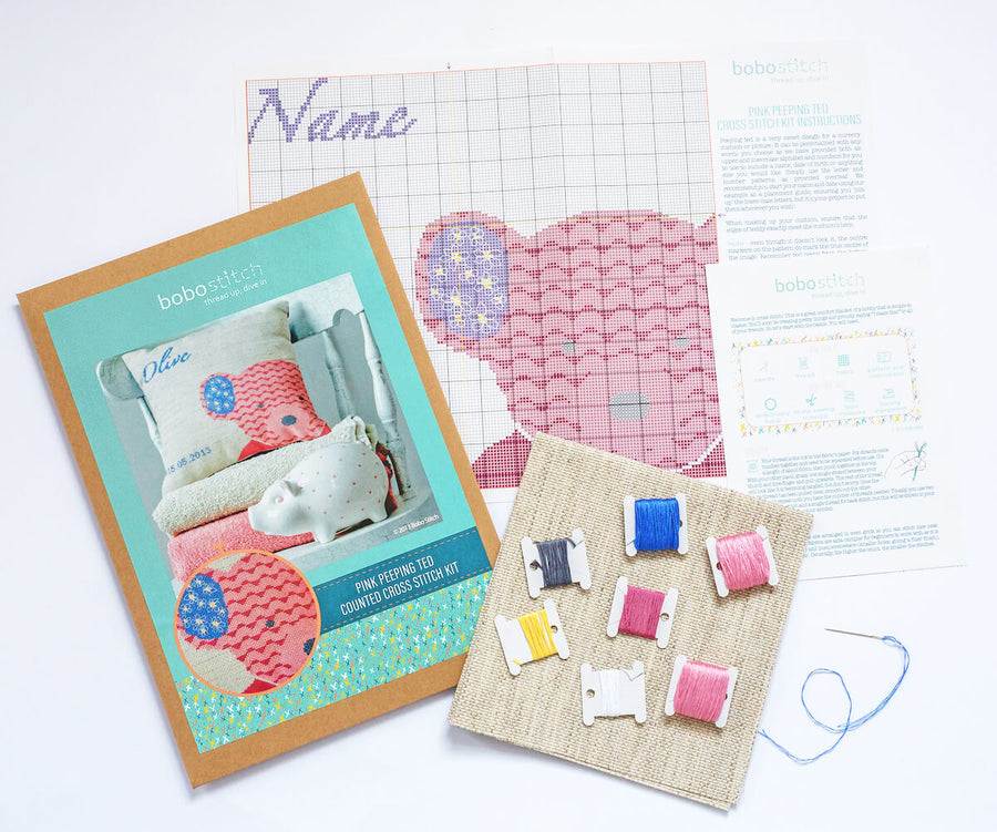 Kit contents for pink teddy cross stitch kit including pattern, fabric and threads.