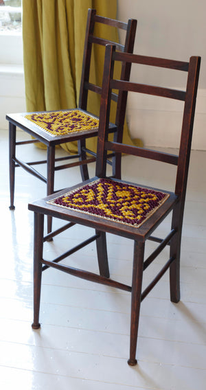 Image from the inside of the book showing two burgundy and gold cross stitched wooden chair bases