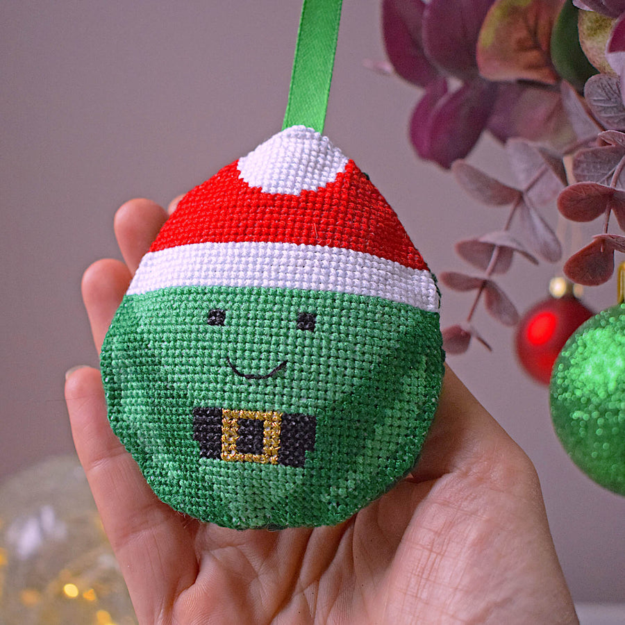 Cross stitched sprout decoration being hung on tree