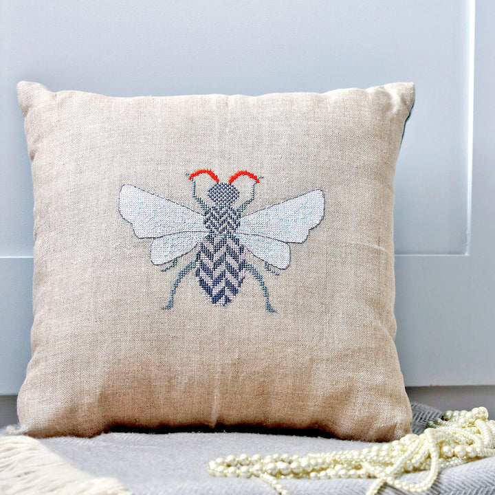 Insect with herringbone patterned body and orange antennae cross stitch design shown made up as a cushion