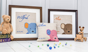 Three colourways of the peeping ted cross stitch kit shown framed or as a cushion, pink, blue and brown