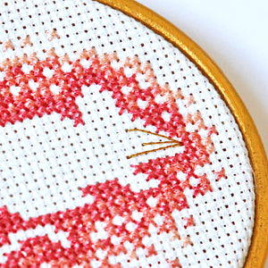 Close up of pink cross stitches around mouse outline with gold whiskers.