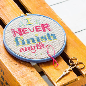 Embroidery hoop filled with slogan saying I never finish anything in pinks and blue/grey stitches with embroidery scissors