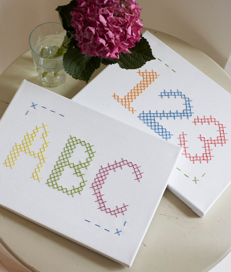 Image from the inside of the book showing two nursery print with large cross stitches saying ABC and 123