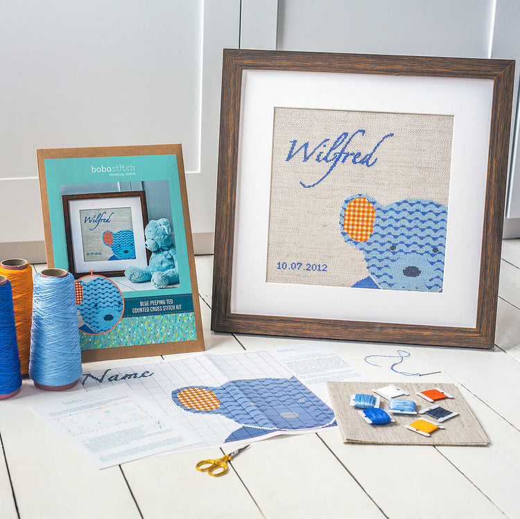 Blue teddy cross stitch design shown framed with threads, pattern and fabric