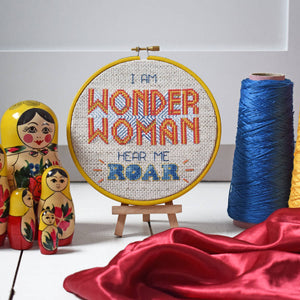 Embroidery hoop with Wonder Woman Hear Me Roar cross stitched inside, with Russian dolls and threads