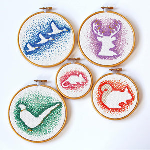 Five negative space cross stitch designs including pink mouse, blue flying ducks, green pheasant, purple stag and orange squirrel